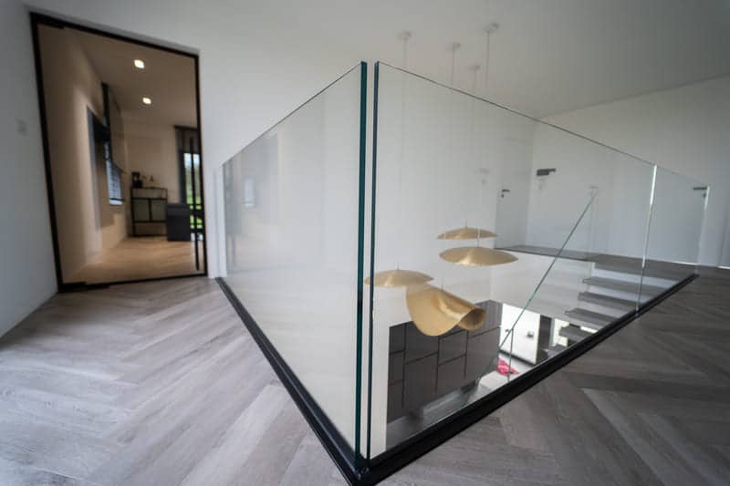 Garde-corps en verre autour d'une cage d'escalier et porte Steel Look noire au fond d'un couloir, maison à Wégimont