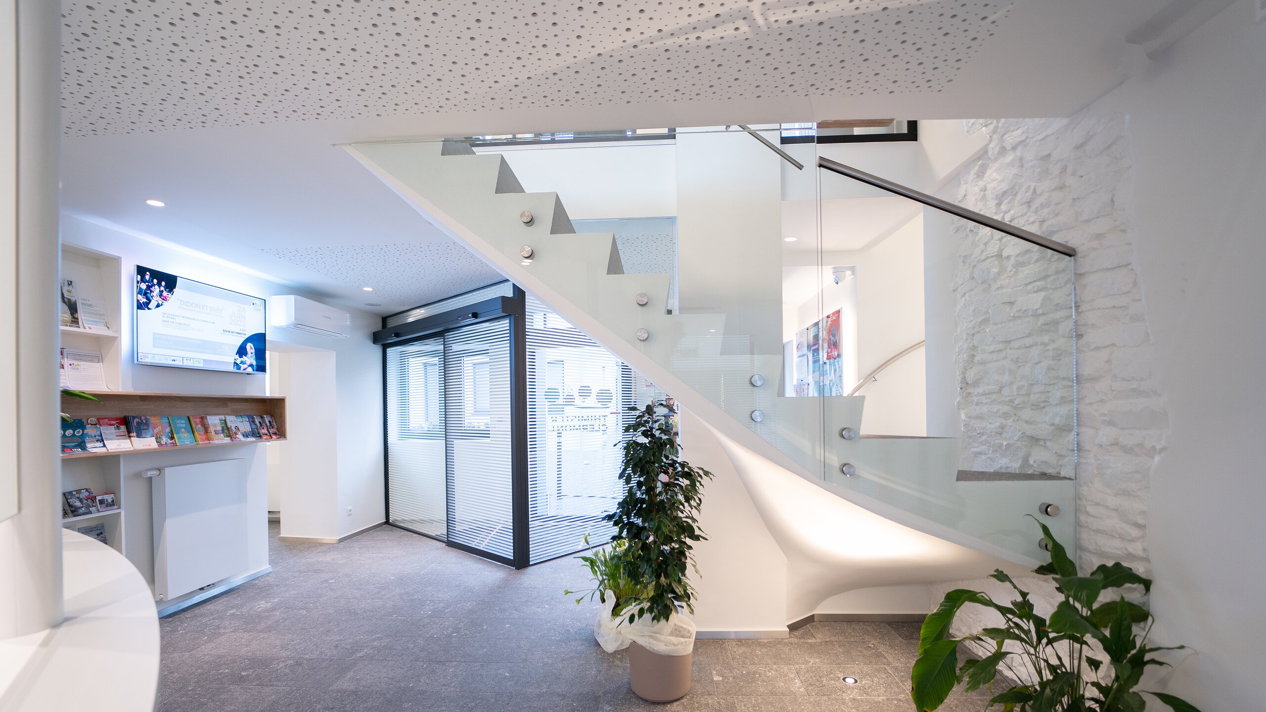 Escalier du hall d'entrée bordé d'un garde-corps en verre à fixations ponctuelles inox, mur de pierre blanche