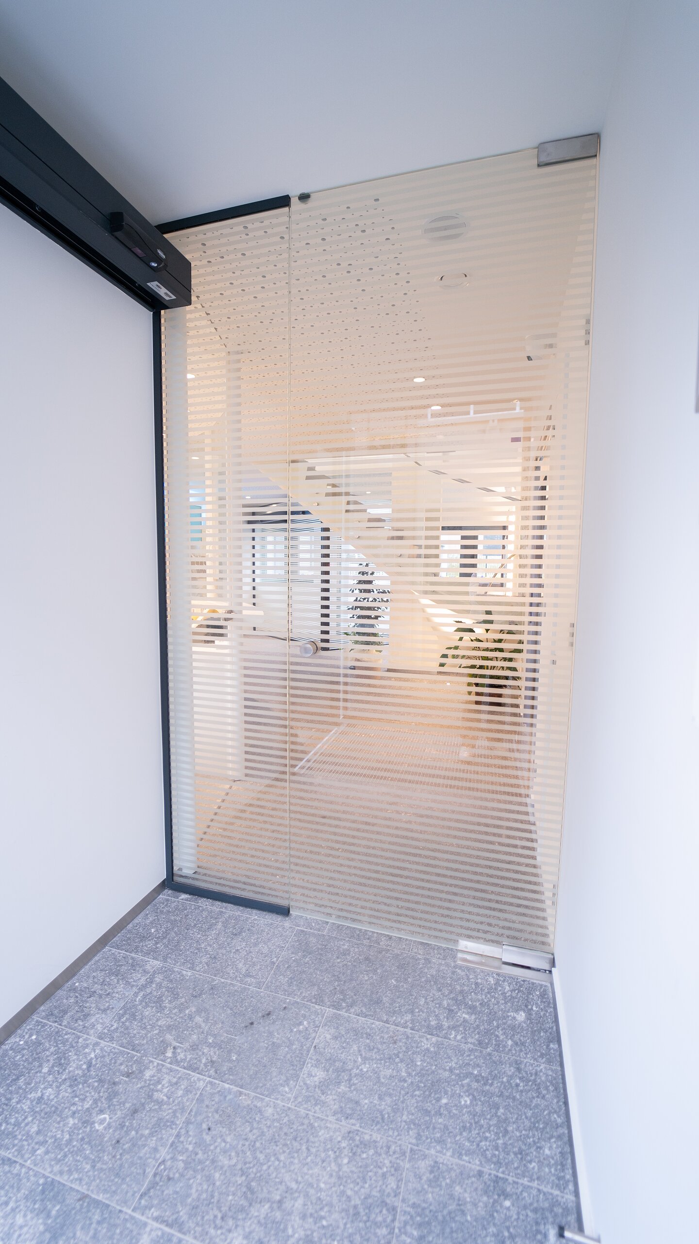 Porte en verre à bandes dépolies ouverte sur un couloir, sol en pierre bleue au premier plan