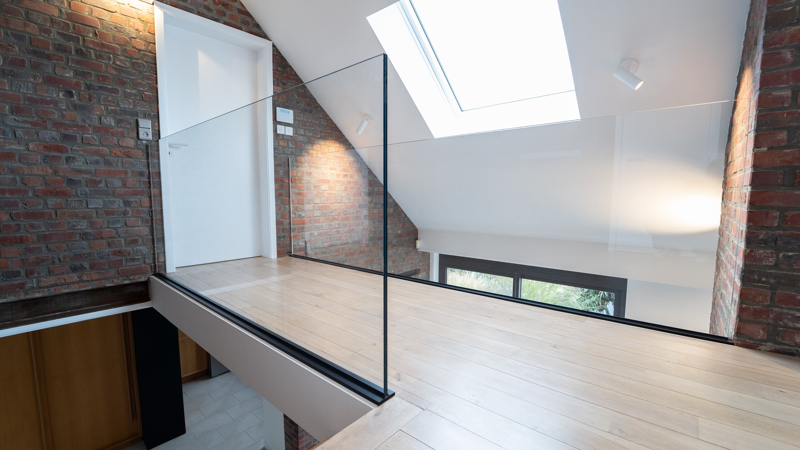 Angle de garde-corps en verre sur profil au sol noir, en bord de mezzanine en chêne sous un velux, briques