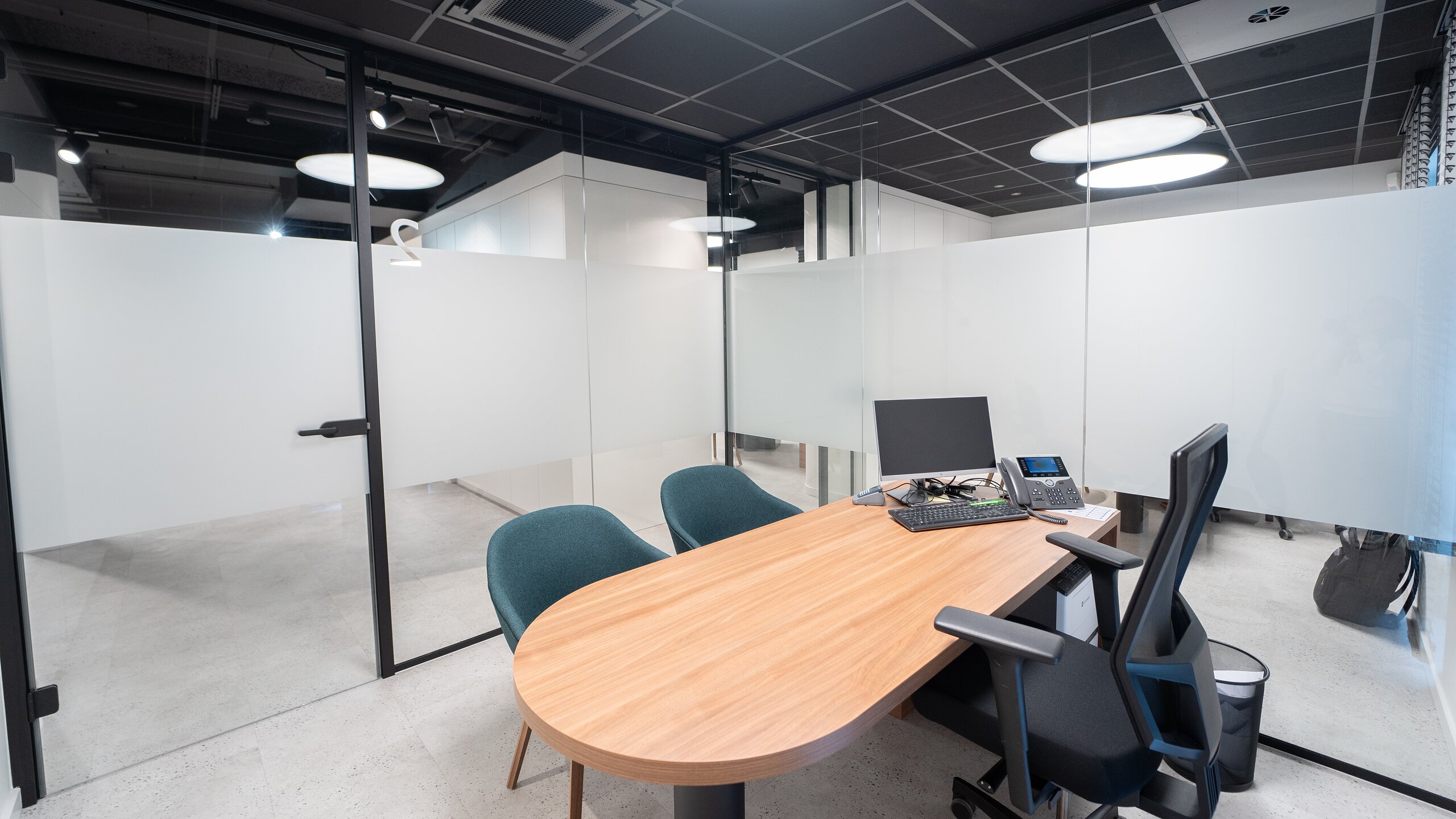 Bureau de conseil entouré de cloisons vitrées dépolies à profilés noirs, table ovale en bois et chaises vertes