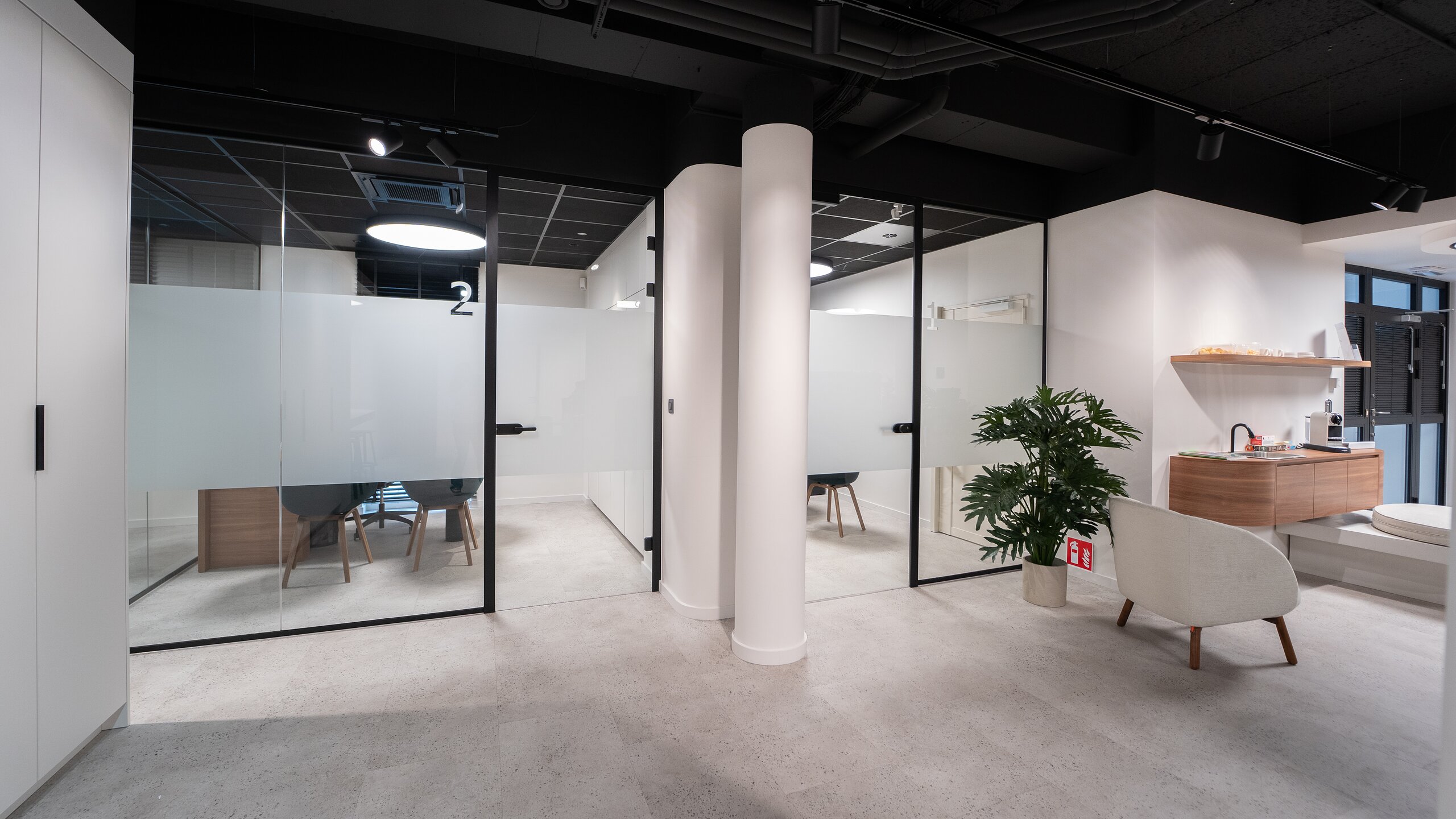 Cloisons vitrées à profilés noirs et bande dépolie autour d'un plateau de bureaux ouvert avec colonne blanche