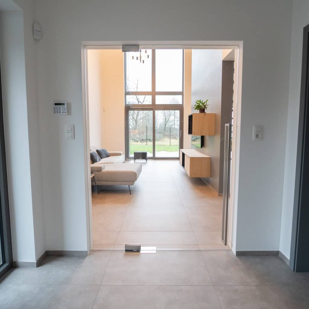 Porte en verre sur pivot fermée, vue frontale sur le salon et ses grandes baies vitrées