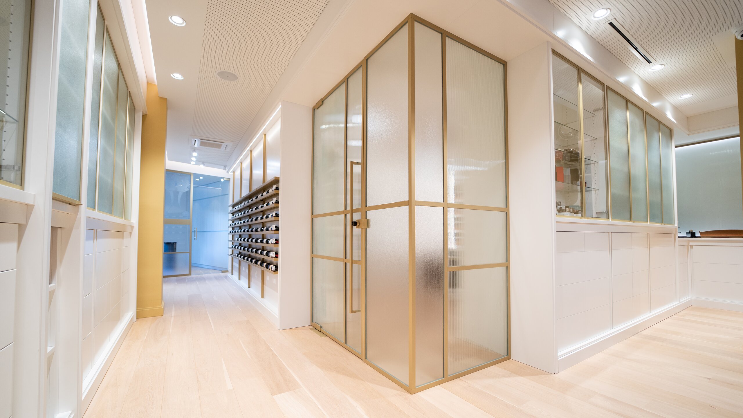 Cabine vitrée à profilés dorés et verre cannelé au cœur d'une boutique claire au parquet de chêne