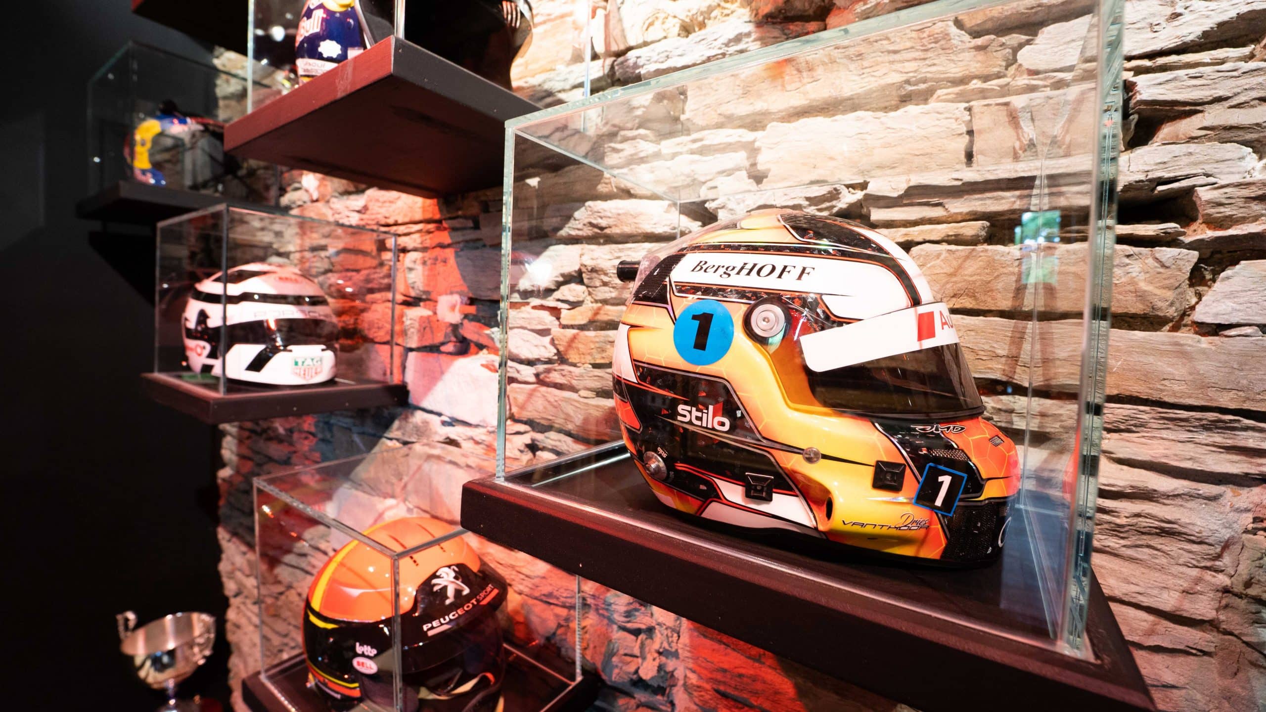 Casque de course exposé dans une vitrine en verre devant un mur en pierre