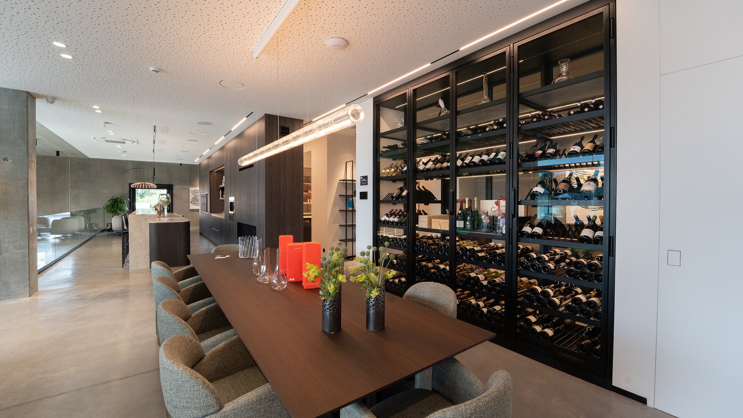 Cave à vin vitrée toute hauteur à cadre noir derrière une longue table de dégustation en bois