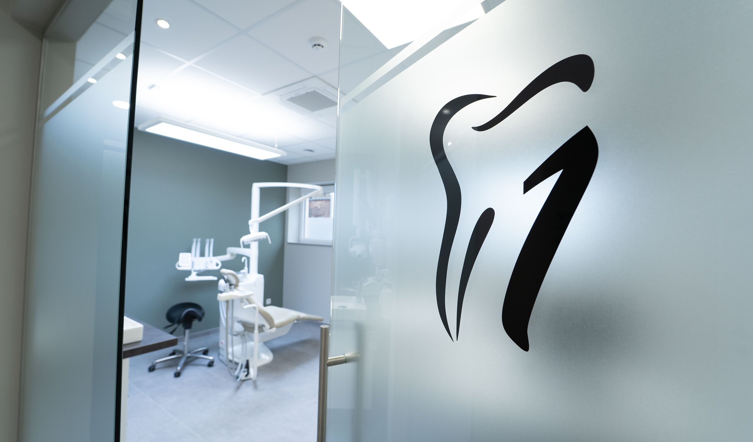 Logo de dent noir sur cloison en verre satiné, avec le cabinet de soins dentaires visible par la partie claire