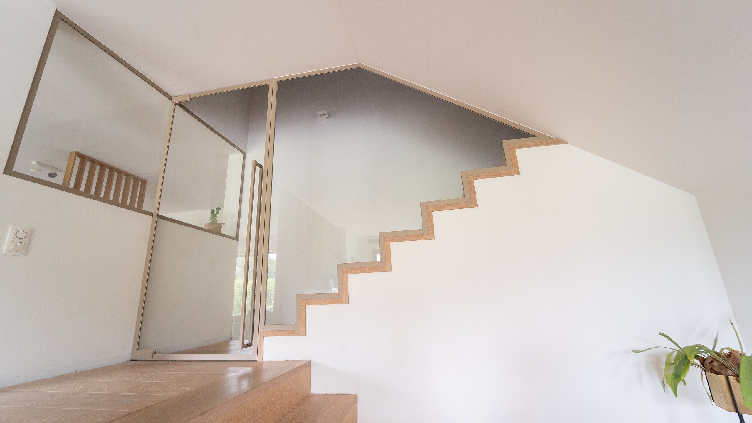 Cloison vitrée à cadre bronze suivant la cage d'un escalier en chêne dans une maison lumineuse