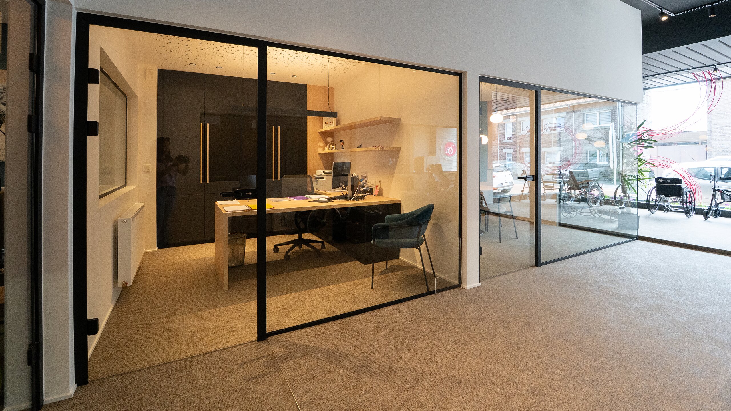Bureau fermé par une cloison vitrée à profilés noirs et porte battante en verre dans un showroom lumineux