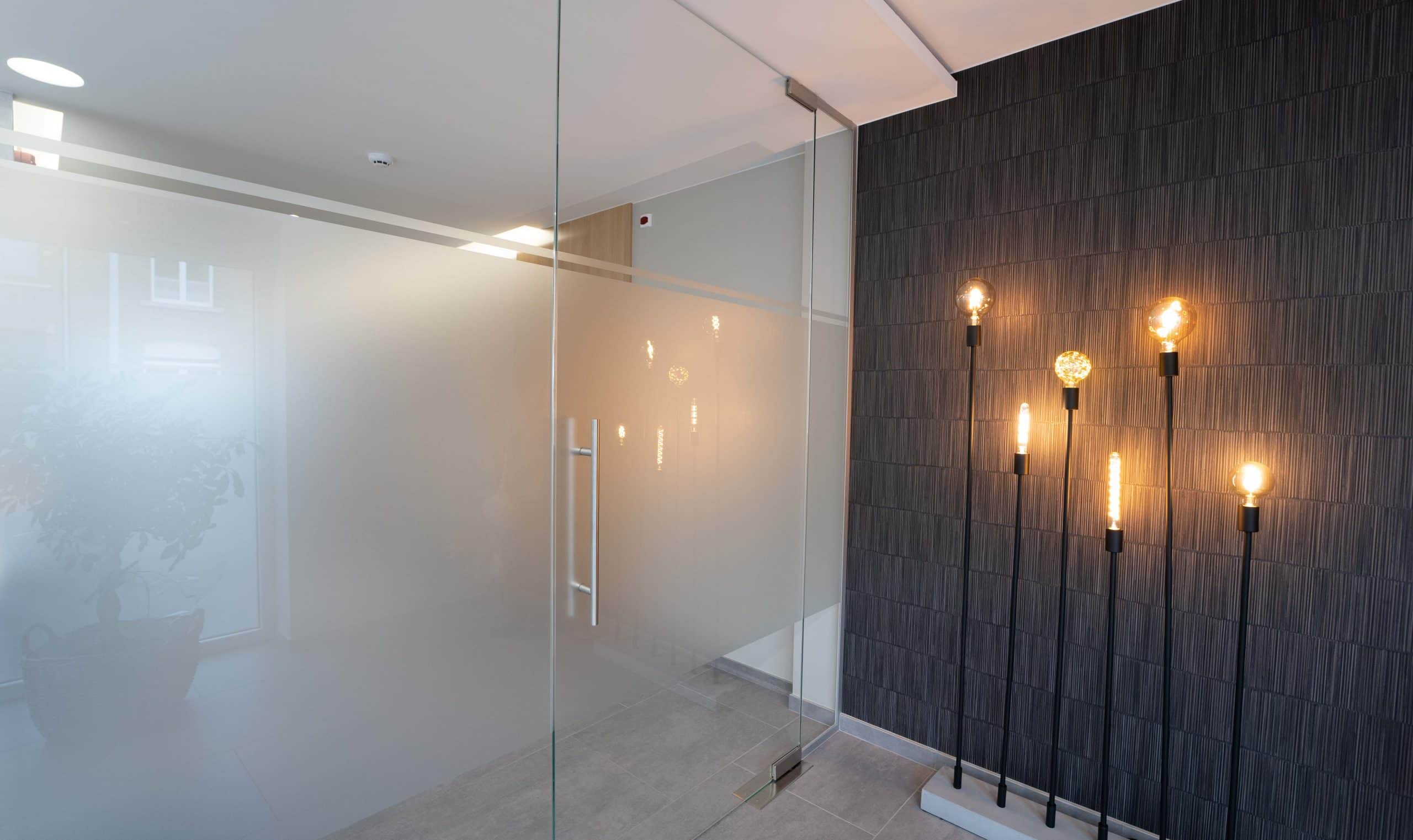 Cloison et porte en verre sablé devant un mur noir