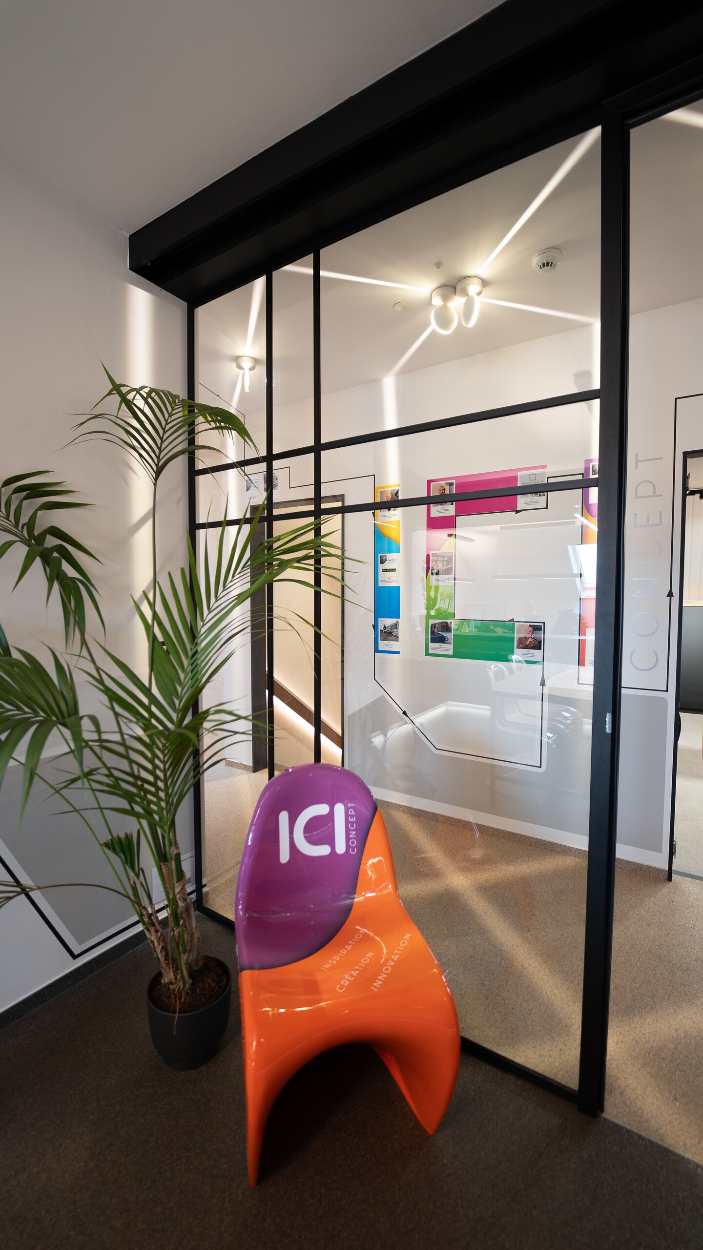 Cloison vitrée steel look à croisillons noirs avec porte, logo ICI sur le verre et chaise design orange devant