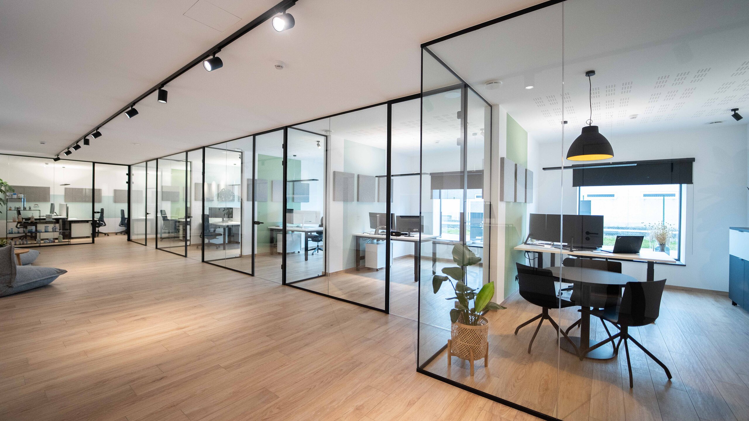 Enfilade de bureaux fermés par des cloisons vitrées à fins profilés noirs, salle de réunion d'angle au premier plan