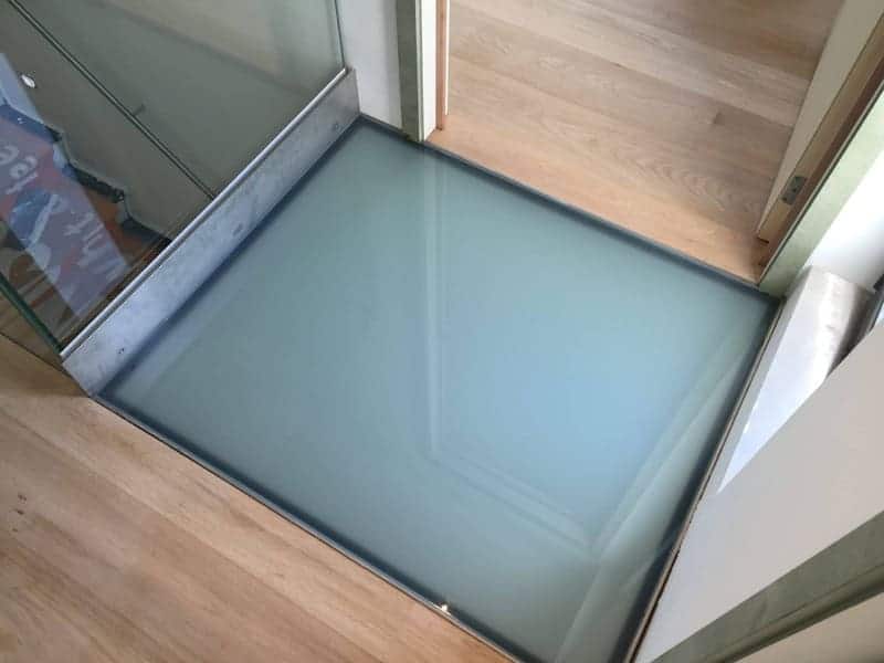 Dalle sablée posée dans un parquet, à côté d'une paroi vitrée