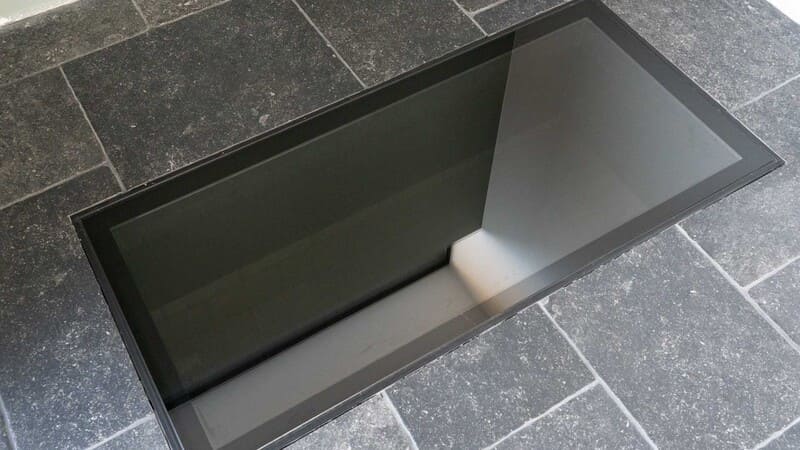 Dalle de sol en verre à bord sombre insérée dans un sol en pierre
