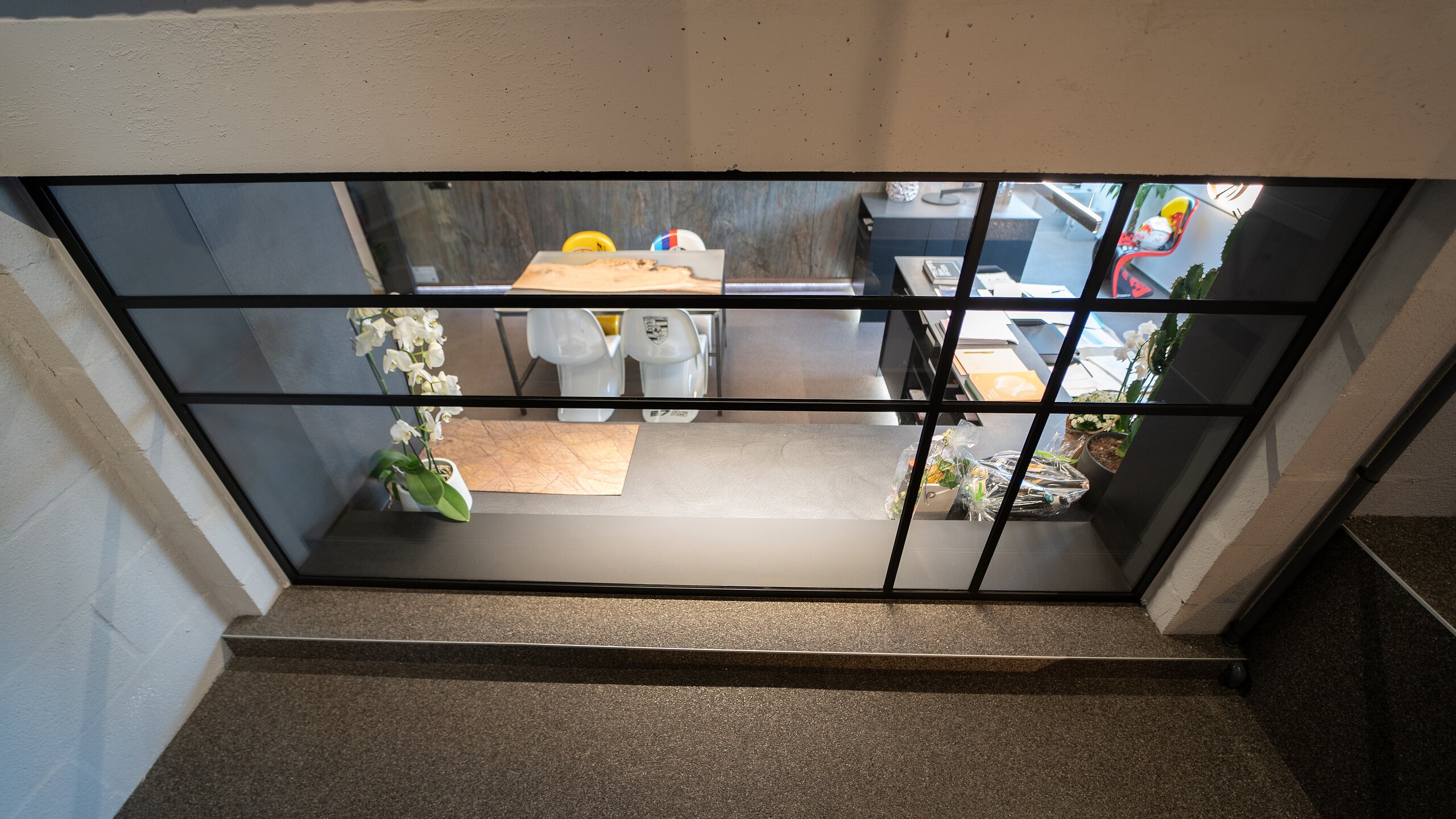 Fenêtre intérieure à profilés noirs façon atelier vue de la mezzanine, donnant sur un bureau aménagé en contrebas