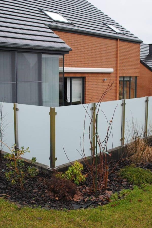 Panneaux de verre sablé en bordure de jardin, protégeant une maison en briques du vis-à-vis