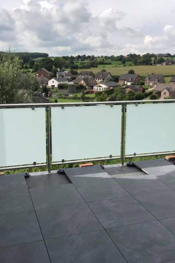 Garde-corps en verre sablé sur une terrasse carrelée, avec vue sur le village en contrebas