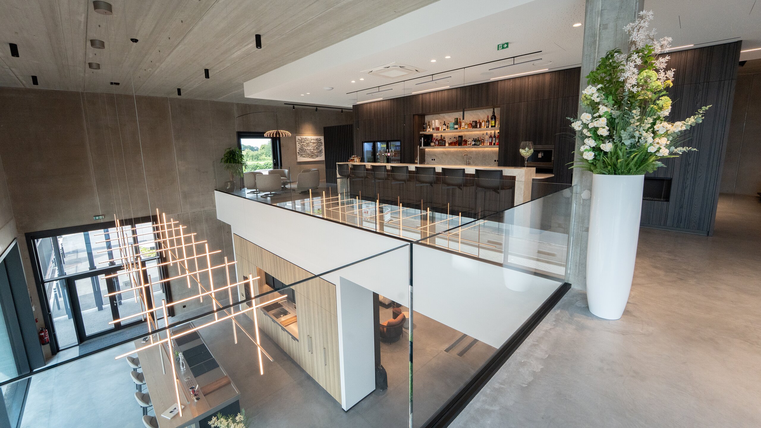 Garde-corps en verre sans montant surplombant le double volume d'un showroom de cuisines avec luminaires