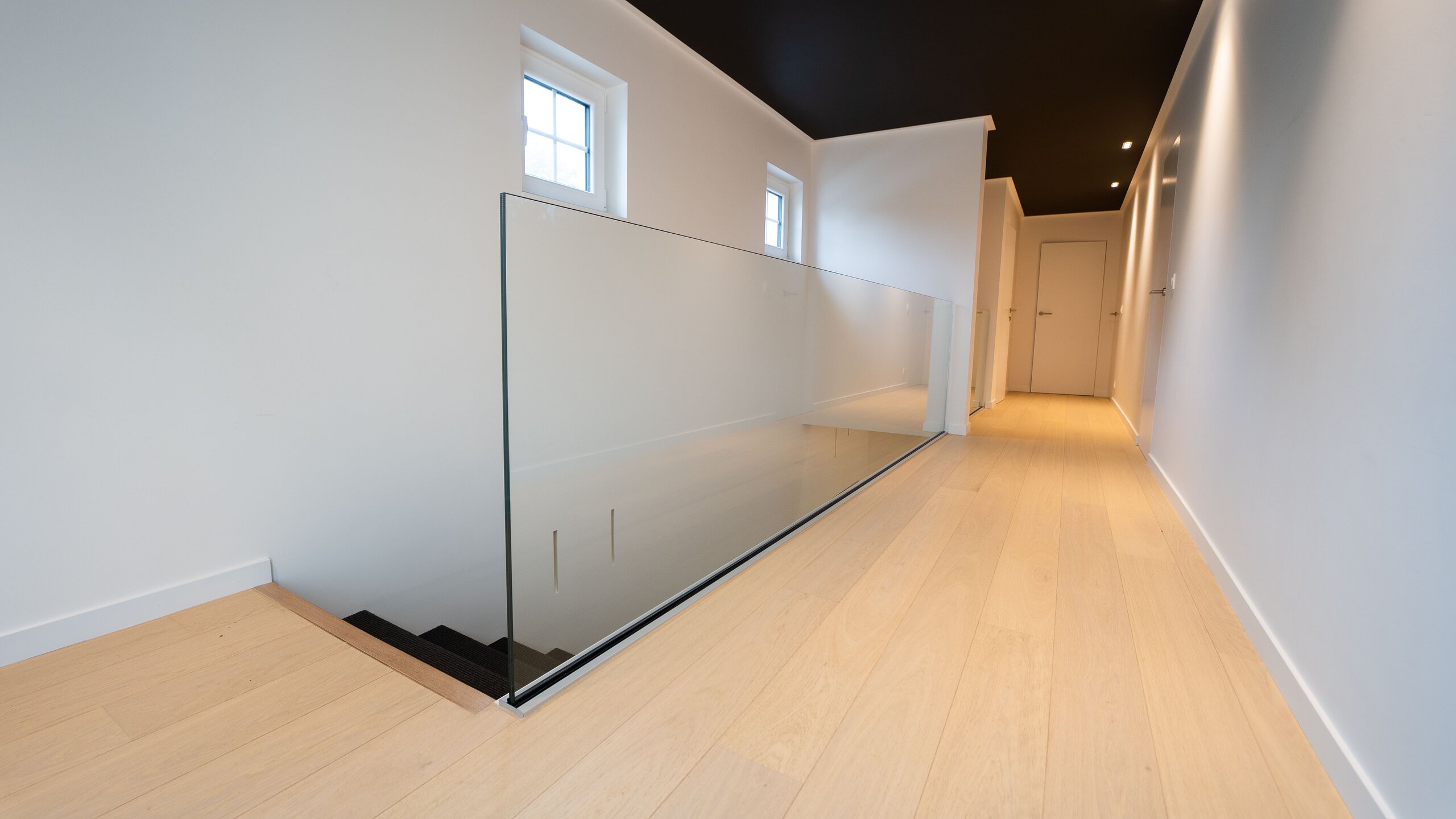 Garde-corps en verre sur profil au sol autour d'une trémie d'escalier, dans un couloir en chêne clair