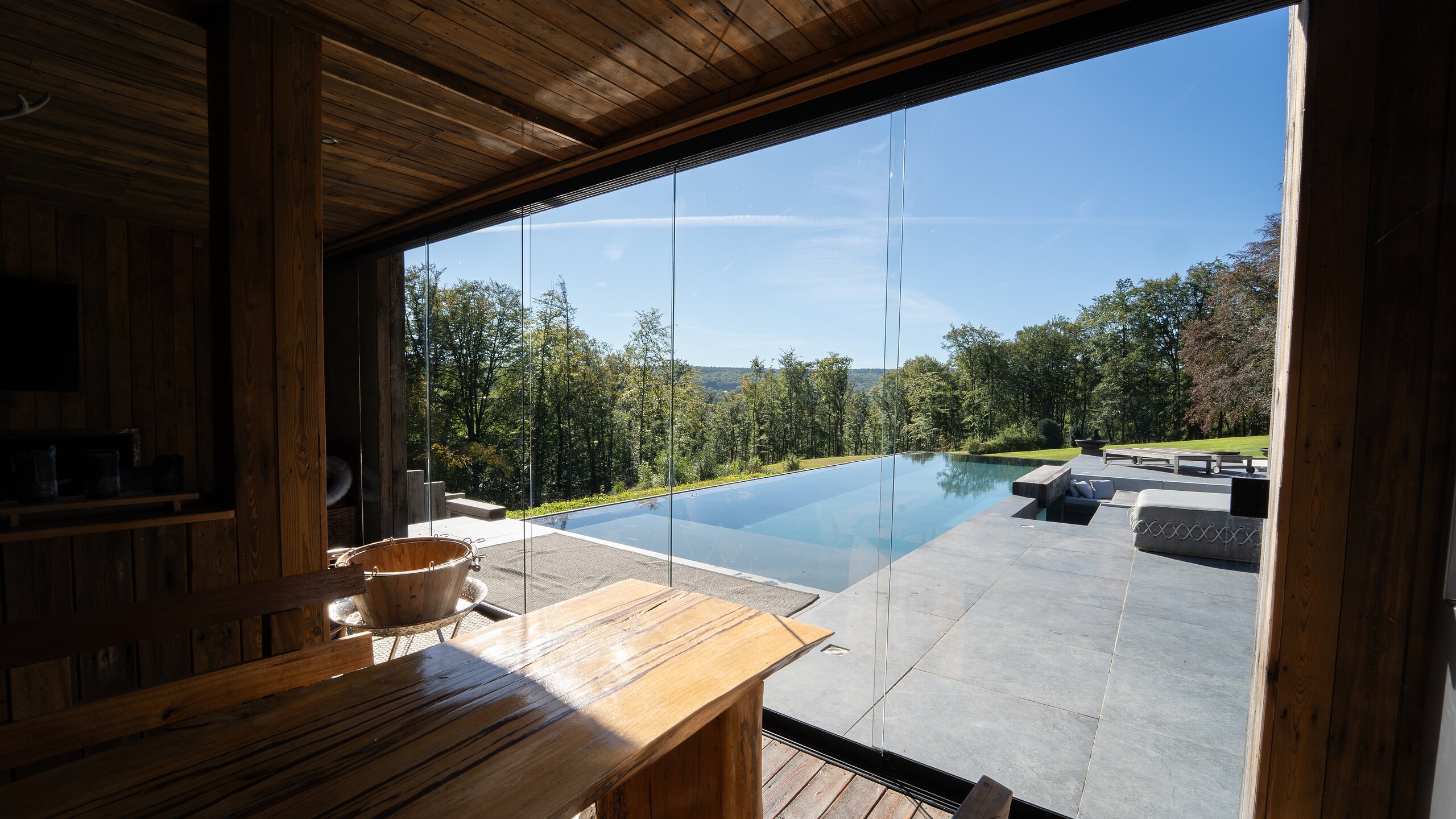 Vue depuis l'intérieur d'un pool house en bois à travers des panneaux vitrés coulissants vers une piscine à débordement