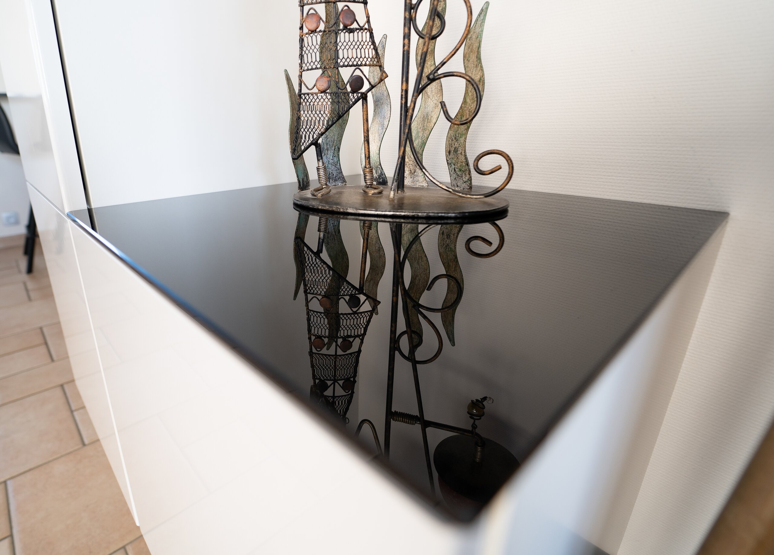 Plateau en verre laqué noir brillant sur un meuble blanc, reflet d’une sculpture en métal dans le verre