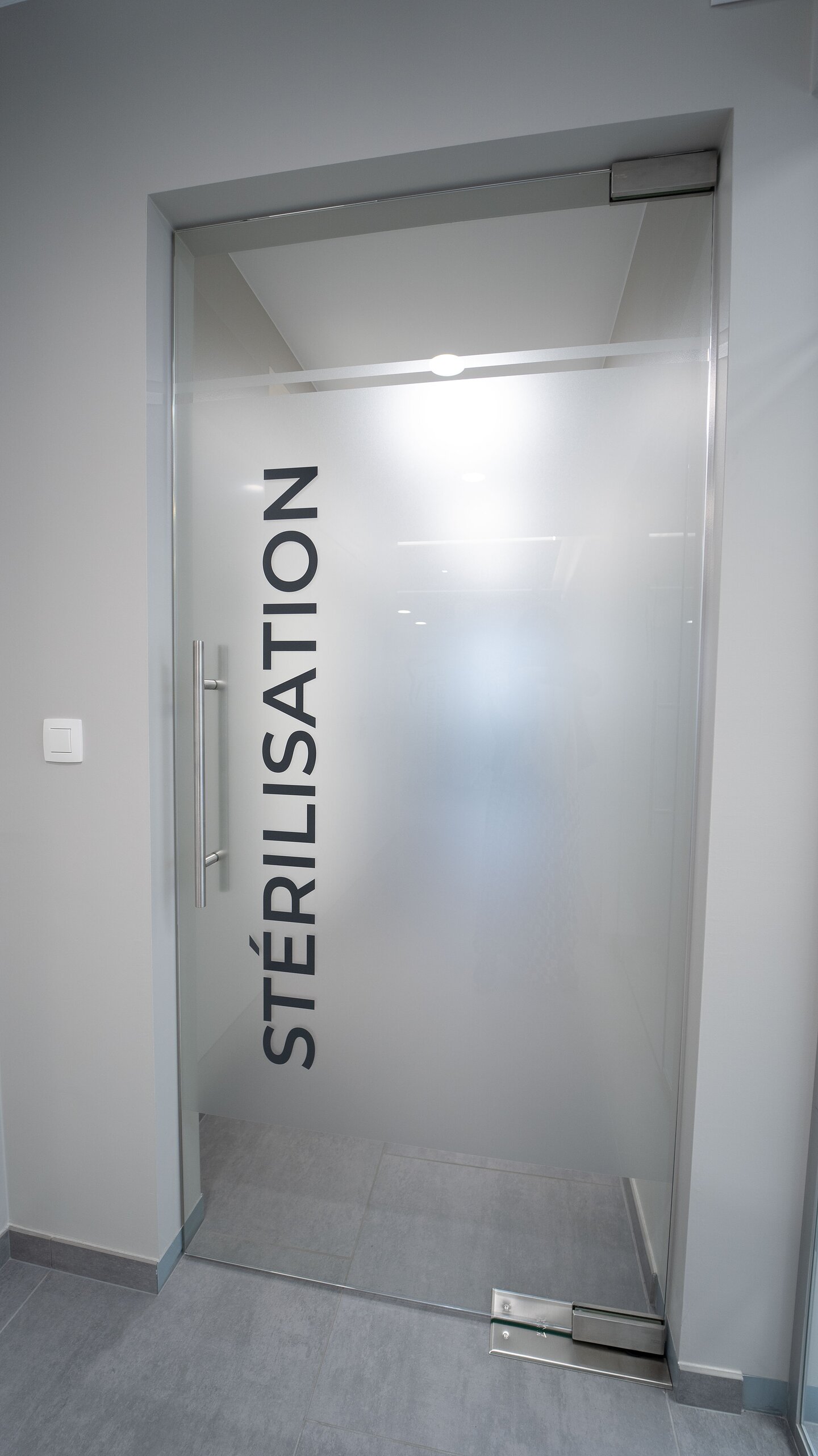 Porte battante en verre dépoli marquée « Stérilisation » en lettres noires, avec poignée inox et pivot au sol