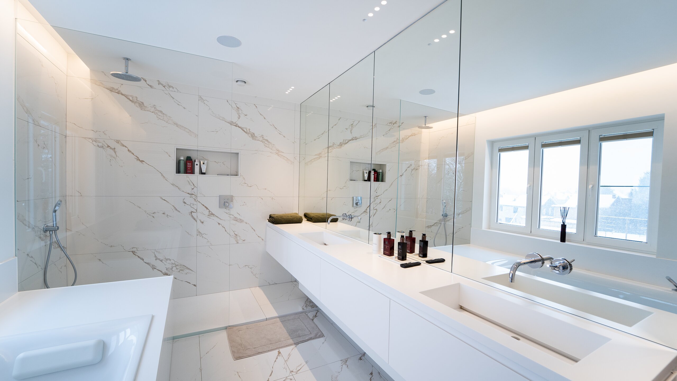 Salle de bain en marbre blanc avec paroi de douche vitrée, grand miroir au-dessus du plan double vasque